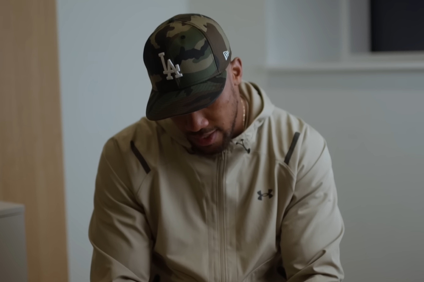 Anthony Joshua cúi đầu trong cuộc phỏng vấn. Ảnh = Cap màn hình YouTube chính thức của Anthony Joshua