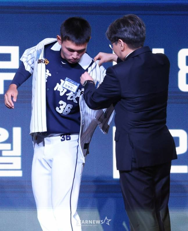 Shin Jae-in (left) is being selected by NC as the second overall pick in the 2026 KBO Rookie Draft and is being handed the NC uniform by Lim Sun-nam and trying it on. /Photo = Kim Jin-kyung on standby
