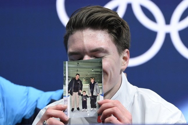 Maxim Naumov holds a picture of himself with his parents at the Kiss and Cry Zone after the men's single free skating event at the 2026 Milan/Cortina D'Ampezzo Winter Olympics at the Milan Ice Skating Arena on the 13th (local time). /AFPBBNews=News1