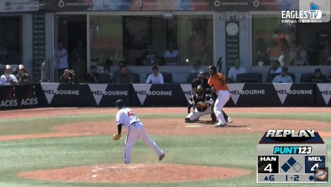 Huh Min (trái) đang ném bóng trước Hanwha Han Ji Yoon. Quả bóng bay cao đang vẽ một đường parabola lớn và rơi về phía người bắt bóng. Ảnh = Cap màn hình phát sóng Eagles TV