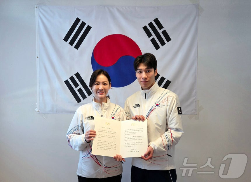 黄大憲（ファン·デホン、右）が15日（韓国時間）、イタリア·ミラノで李スギョン選手団長から李在明（イ·ジェミョン）大統領の祝電を受けた後、記念撮影をしている。 左から2026ミラノ·コルティナダンペッツォ冬季五輪大韓民国選手団団長のイ·スギョン、ショートトラック男子1500メートル銀メダリストのファン·デホン。 /写真=ニュース1提供  