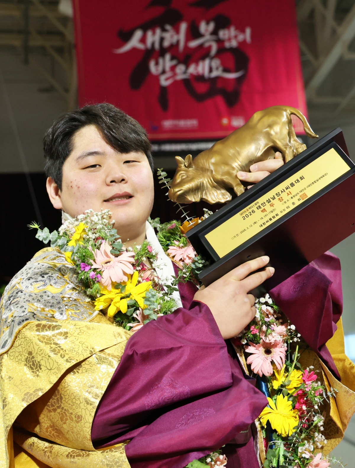 Kim Min-jae (Yeongam-gun Folk Ssireum Team), who was crowned Baekdu Jangsa (140kg or less) at Withers Pharmaceutical 2026 Taean Lunar New Year Ssireum Competition at Taean Indoor Gymnasium in Taean-gun, Chungcheongnam-do, is taking a commemorative photo with a business certificate and a bull trophy. /Photo = Courtesy of the Korea Wrestling Association