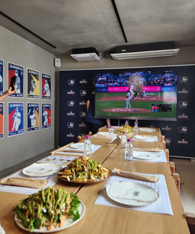 1日に行われた「MLBブレックファーストクラブ(MLB Breakfast Club)」イベントで、セットされている料理の後ろに中継されているMLBの試合画面。 /写真=アン·ホグン記者