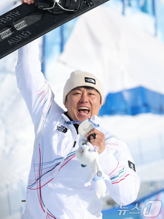 Kim Sang-gyeom is holding a silver medal in his left hand and a snowboard in his right hand while standing on the podium at the men's parallel competition at the 2026 Milan-Cortina D'Ampezzo Winter Olympics held at Lvigno Snowpark in Italy on the 8th (Korea time). /Photo = News 1