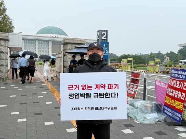 조이웍스 임직원 비상대책위원회 관계자가 지난달 20일 서울 여의도 국회 앞에서 호카 국내 총판 계약 해지에 반발하는 내용의 피켓을 들고 있다.