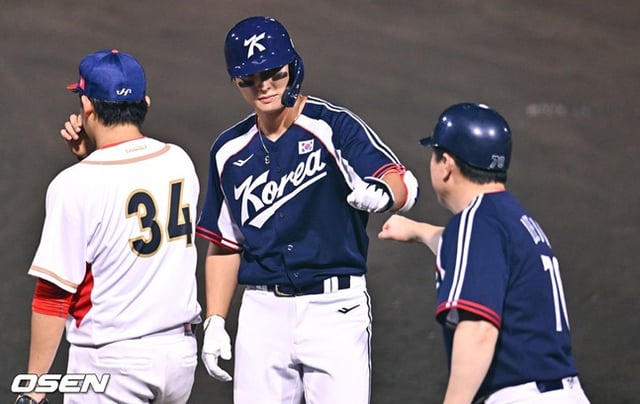 Yoon Dong-hee (centro) de la selección coreana de béisbol conecta un hit de sacrificio con una carrera para sellar el partido en el octavo inning superior del segundo partido de la fase de grupos del Grupo B de los Juegos Asiáticos Aichi-Nagoya 2026 contra Hong Kong, celebrado el día 22 en el estadio municipal de Toyohashi, prefectura de Aichi, Japón, y saluda al entrenador con un abrazo.