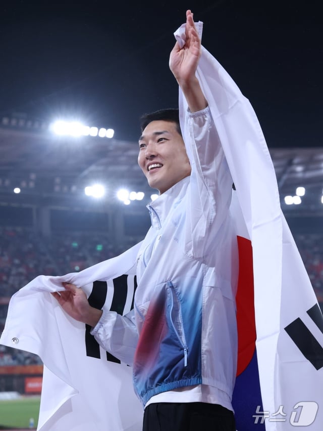 韓国陸上のウ·サンヒョクが27日、名古屋瑞穂公園陸上競技場で開かれた2026愛知·名古屋アジア大会男子走り高跳び銅メダルを確定した後、太極旗を背負ってセレモニーをしている。 /写真=ニュース1提供