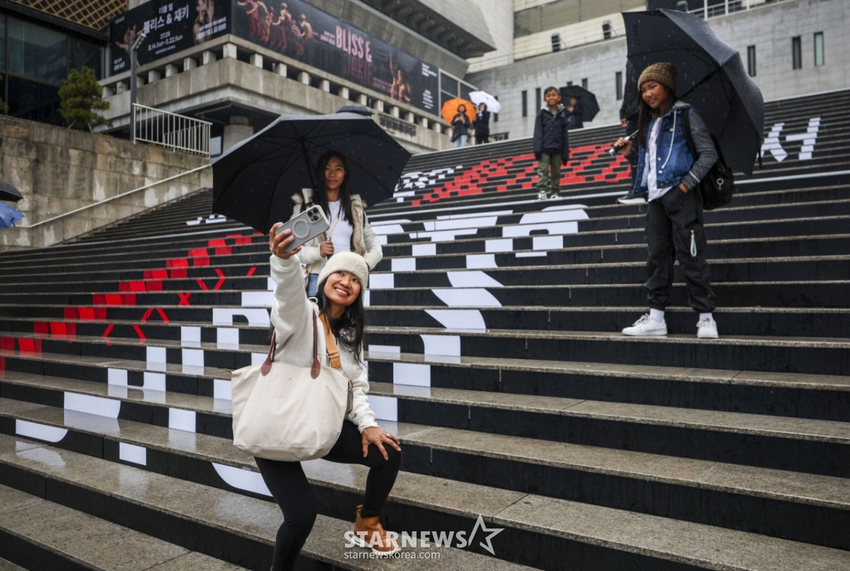 【ソウル=ニューシス】チョン·ビョンヒョク記者=BTS（BTS）のソウル光化門（クァンファムン）広場カムバック公演を控えた18日、ソウル鍾路区世宗（チョンログ·セジョン）文化会館の階段を訪れた外国人ファンがBTSラッピングの前で写真を撮っている。 2026.03.18.jhope@newsis.com /写真=チョン·ビョンヒョク