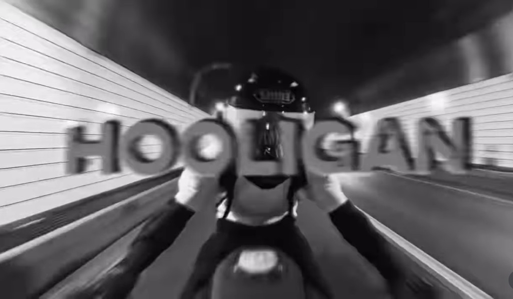 BTS's Jungkook seen from behind on a motorcycle, riding through a city at night for his 'Hooligan' challenge video.