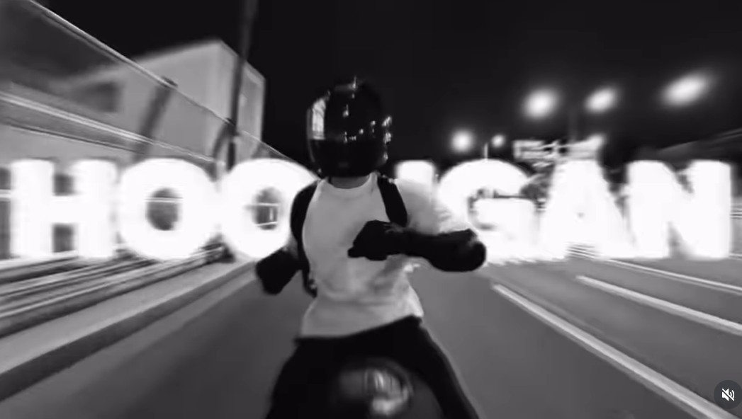 Jungkook of BTS showcasing his riding skills on a motorcycle, momentarily letting go of the handlebars in his 'Hooligan' challenge.