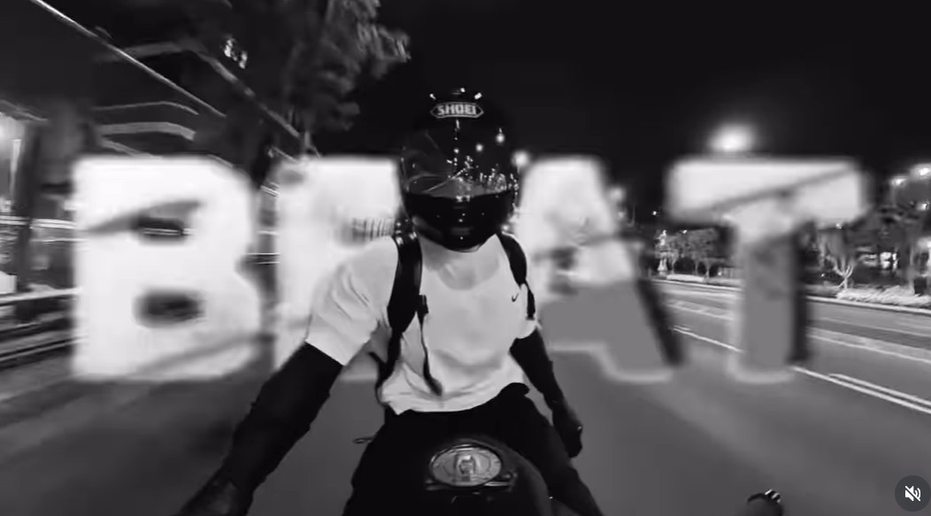 BTS's Jungkook on a motorcycle at night, wearing a cap and helmet, as seen in his viral 'Hooligan' challenge video.